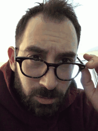 a man with a beard wearing glasses looks at the camera