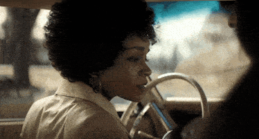 a woman with curly hair is driving a car and looking out the window