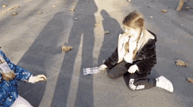 a little girl is sitting on the ground with a bottle of water in her hand .