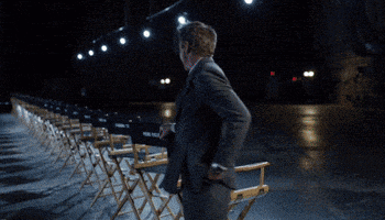 a man in a suit and tie is walking in front of a row of chairs