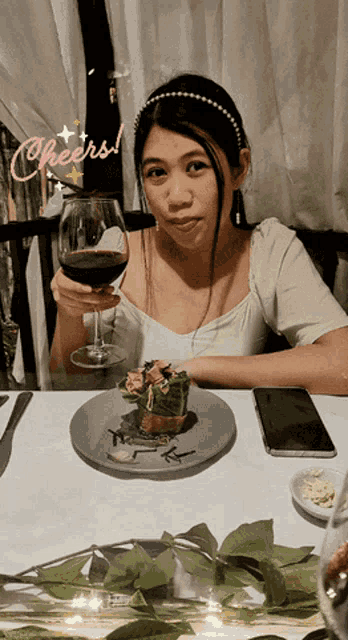a woman sitting at a table with a plate of food and a glass of wine with cheers written on the bottom