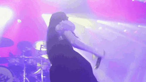 a woman is singing into a microphone on a stage with a drummer in the background