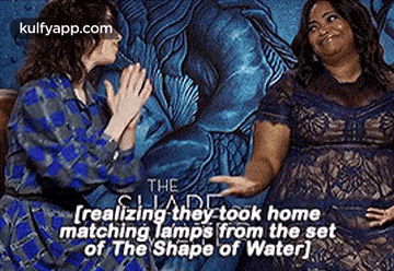 two women are sitting next to each other in front of a painting and talking about the shape of water .