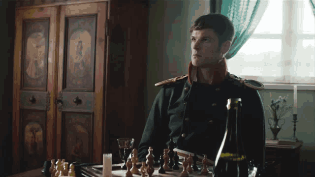 a man in a green uniform sits at a table with a bottle of wine