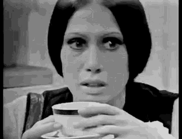 a woman is holding a cup of coffee in her hands and looking at the camera .