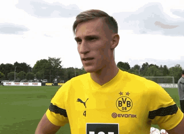 a man wearing a yellow bvb jersey stands on a soccer field