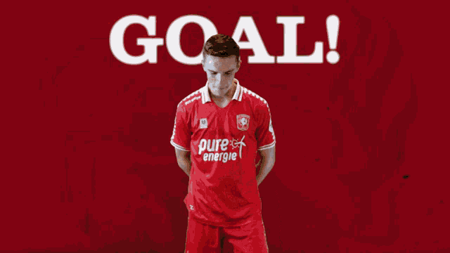 a man in a red pure energie shirt stands in front of a red background that says goal