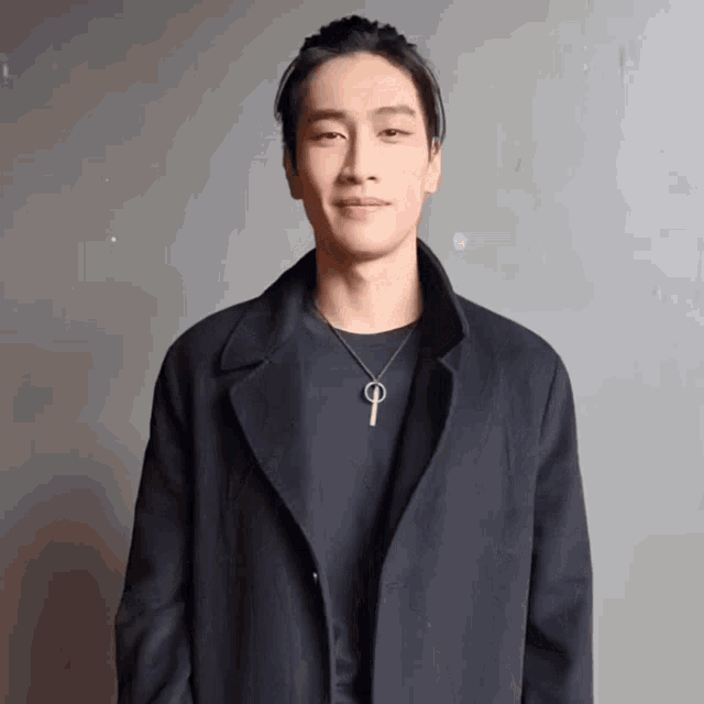 a man wearing a black coat and a necklace with the letter p