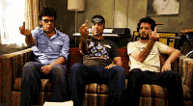 three men are sitting on a couch and one of them is giving the middle finger