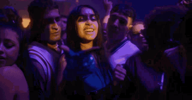 a group of people are dancing in a club with purple lights