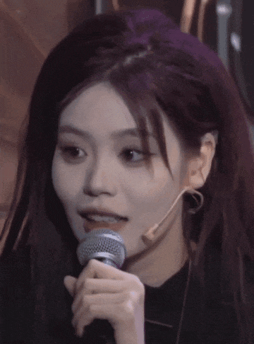 a girl with purple hair is singing into a microphone with chinese writing on it