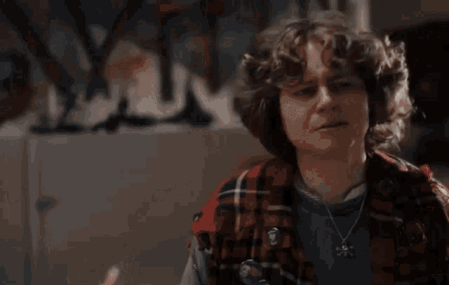 a young man wearing a plaid shirt and a necklace is smiling