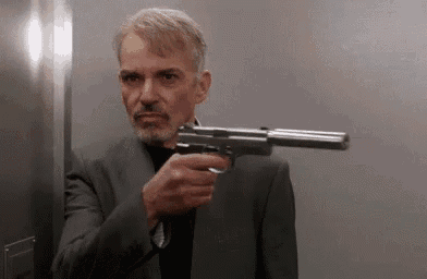 a man in a suit is holding a gun in his right hand .