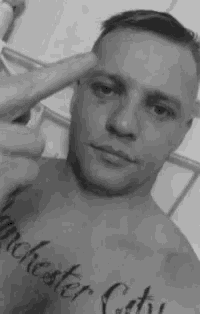 a black and white photo of a shirtless man with a tattoo on his chest .