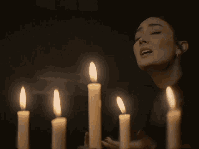 a woman with her eyes closed stands in front of lit candles