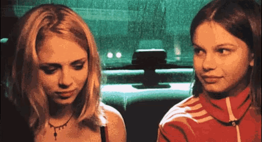 two girls are sitting next to each other in a car and one is wearing a red adidas jacket
