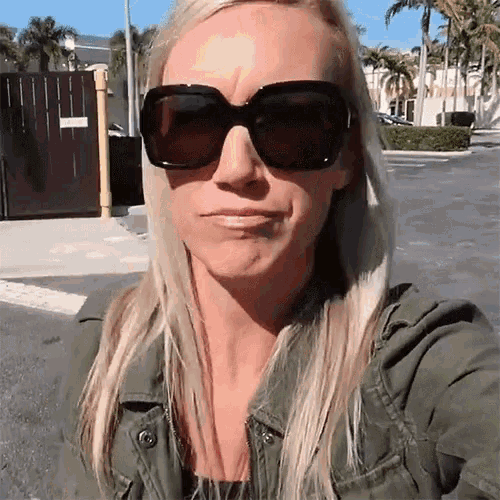 a blonde woman wearing sunglasses and a green jacket