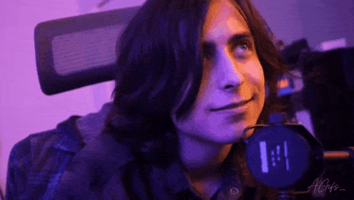 a man with long hair is sitting in a chair in front of a microphone .