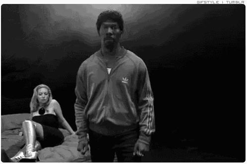 a man wearing an adidas jacket stands in front of a woman on a bed