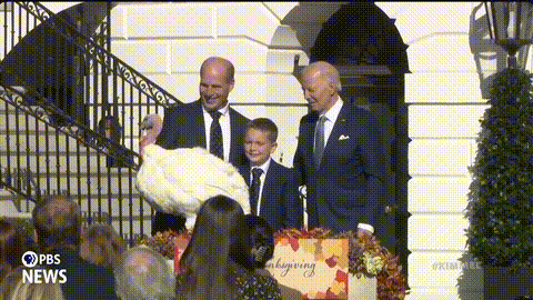 a man in a suit holds a turkey in front of a sign that says " thanksgiving "