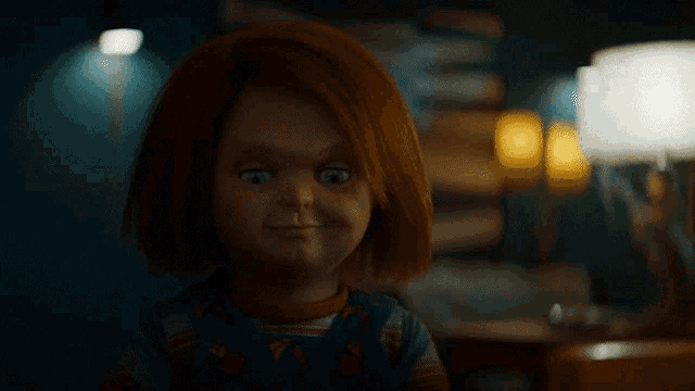 a doll with red hair is smiling in a dark room with a lamp in the background