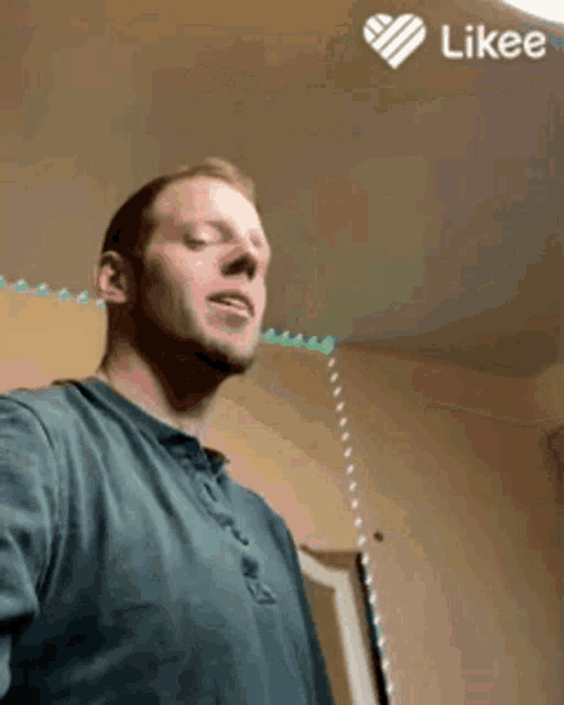 a man in a blue shirt is taking a selfie with a likee heart in the corner