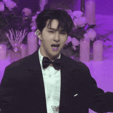 a man in a tuxedo and bow tie is standing in front of candles and flowers