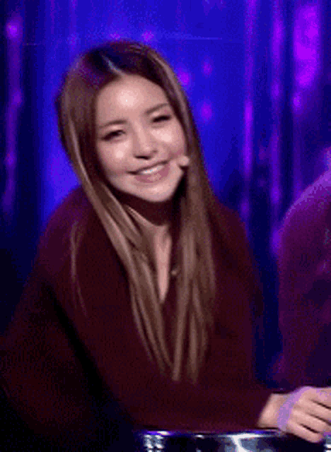 a woman in a maroon sweater is laughing in front of a purple background