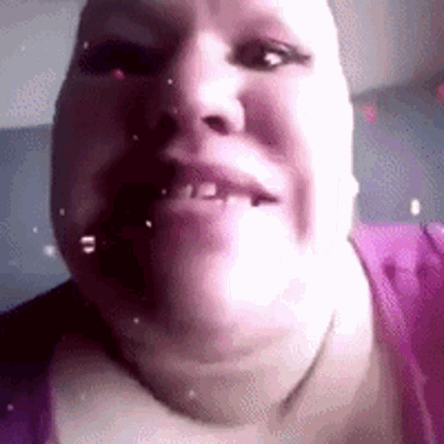 a close up of a woman 's face with a purple shirt on making a funny face .