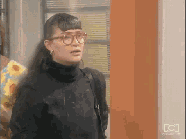 a woman wearing glasses and a black turtleneck sweater is standing in front of a window .