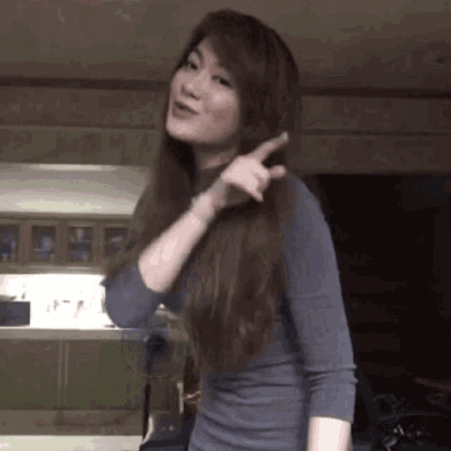 a woman is pointing at her hair while wearing a grey shirt .