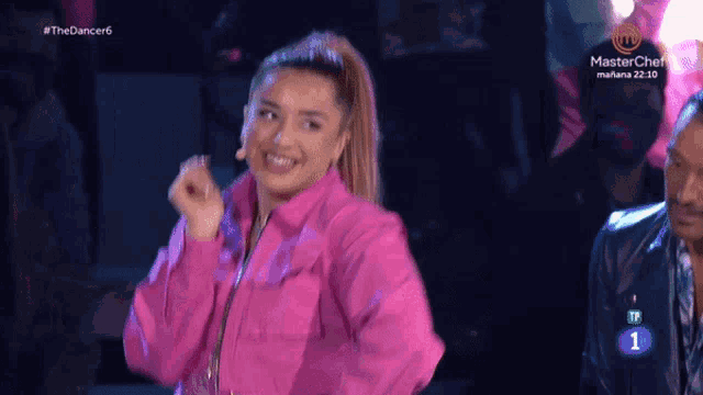 a woman in a pink jacket is dancing in front of a screen that says masterchef