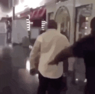 a man in a white shirt is walking down a hallway while a man in a black shirt stands behind him .