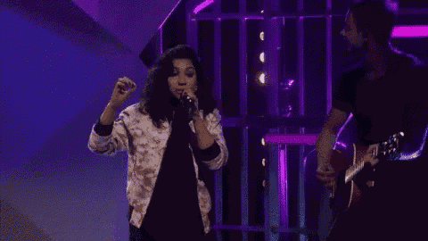 a woman is singing into a microphone while a man plays a guitar in a dark room .