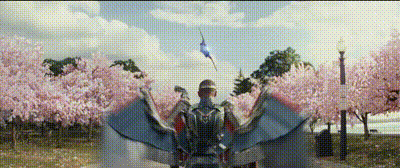 a man in a superhero costume is flying through a park with cherry blossom trees .