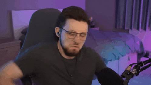 a man wearing glasses is sitting in front of a microphone and making a face