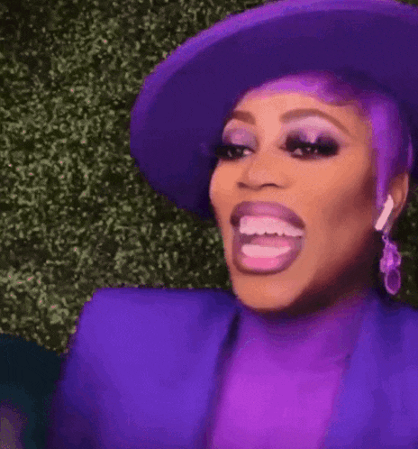 a woman with purple hair and a purple hat is making a funny face with her mouth open .