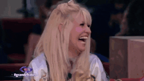a blonde woman is laughing while holding a dog in her lap .