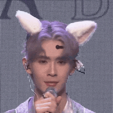 a young man wearing bunny ears is holding a microphone and singing into it .