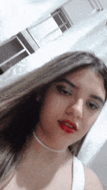 a woman wearing a white tank top and red lipstick looks at the camera