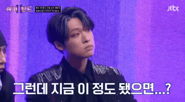 a man in a black shirt is sitting in front of a purple screen with korean writing .