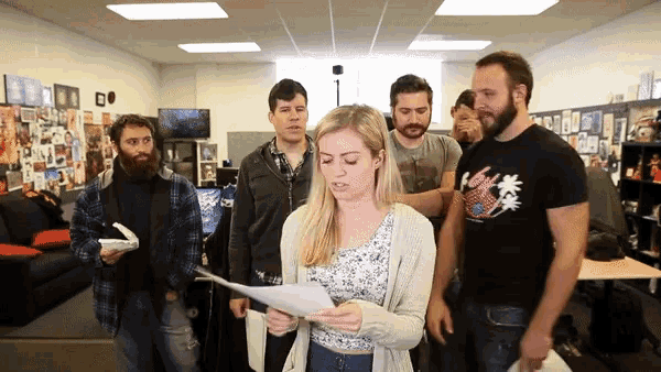 a group of people are standing around a woman reading a paper