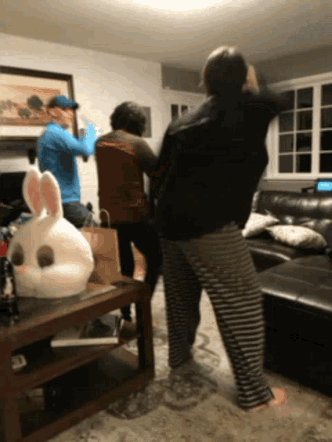 a group of people dancing in a living room with a rabbit mask on a table