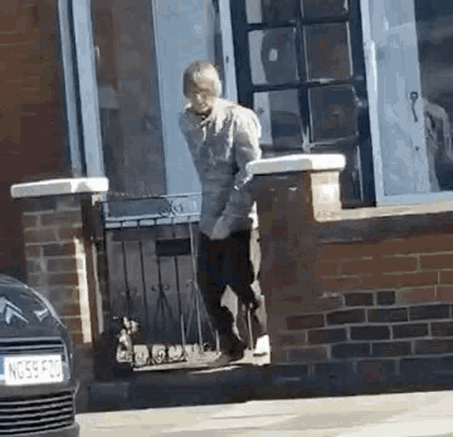 a man is walking down a sidewalk in front of a brick house .