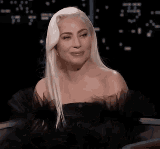 lady gaga is wearing a black dress and smiling while sitting in a chair .