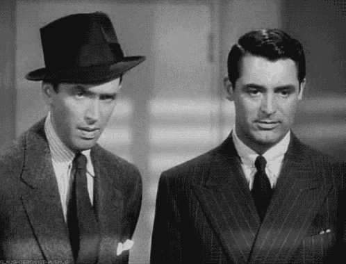 a black and white photo of two men in suits and hats standing next to each other .
