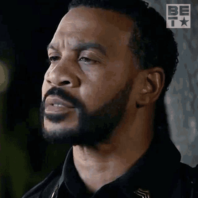 a close up of a man 's face with a beard and a be logo in the background