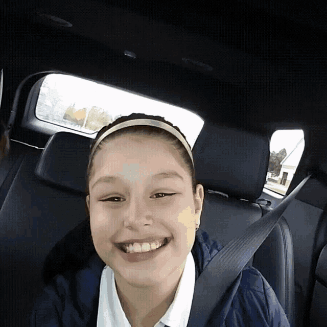 a young girl wearing a headband is smiling while sitting in the back seat of a car