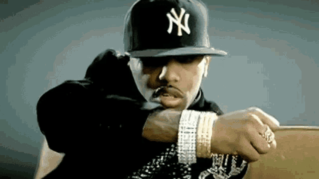 a man wearing a ny hat and a lot of bracelets is sitting in a chair .