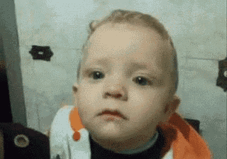 a baby is making a funny face while sitting in a chair .